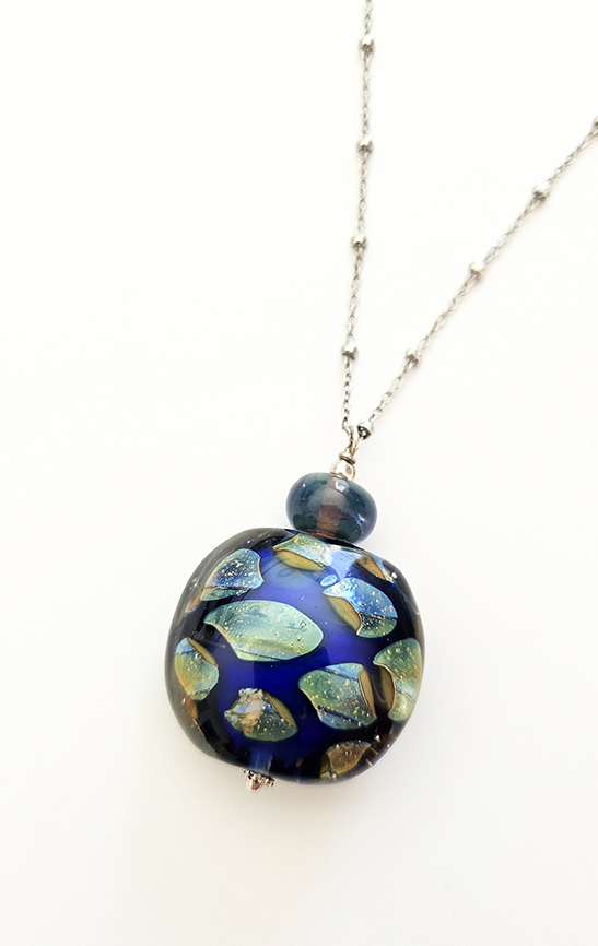 Gros plan du pendentif bleu "éclats de nuit" en verre de Murano avec éclats iridescents