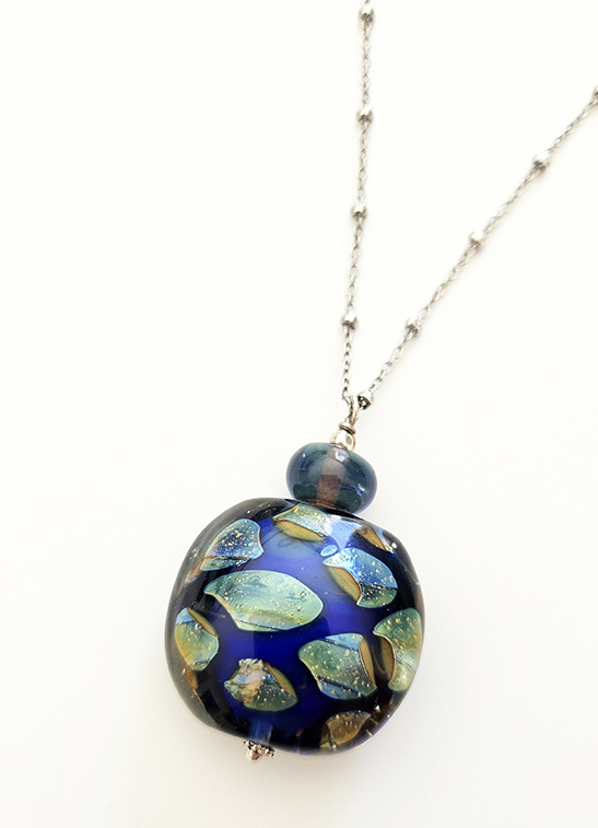 Gros plan du pendentif bleu "éclats de nuit" en verre de Murano avec éclats iridescents